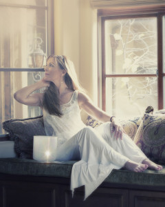 A woman sitting on the couch in front of a window.