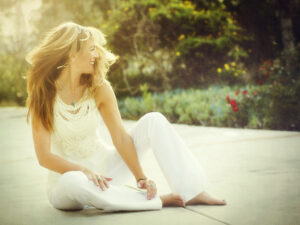 Woman sitting outdoors, smiling in sunlight.